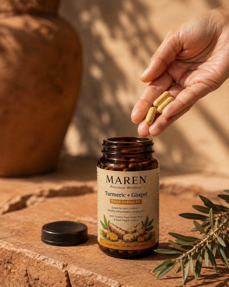 Hand dropping MAREN turmeric and ginger capsules into the open bottle, terracotta background